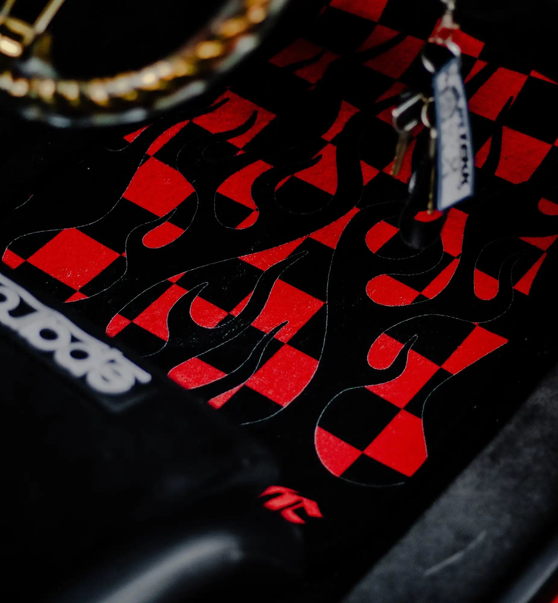 Red and black checkered skateboard grip tape with white text ’scoot’ on a glossy surface.